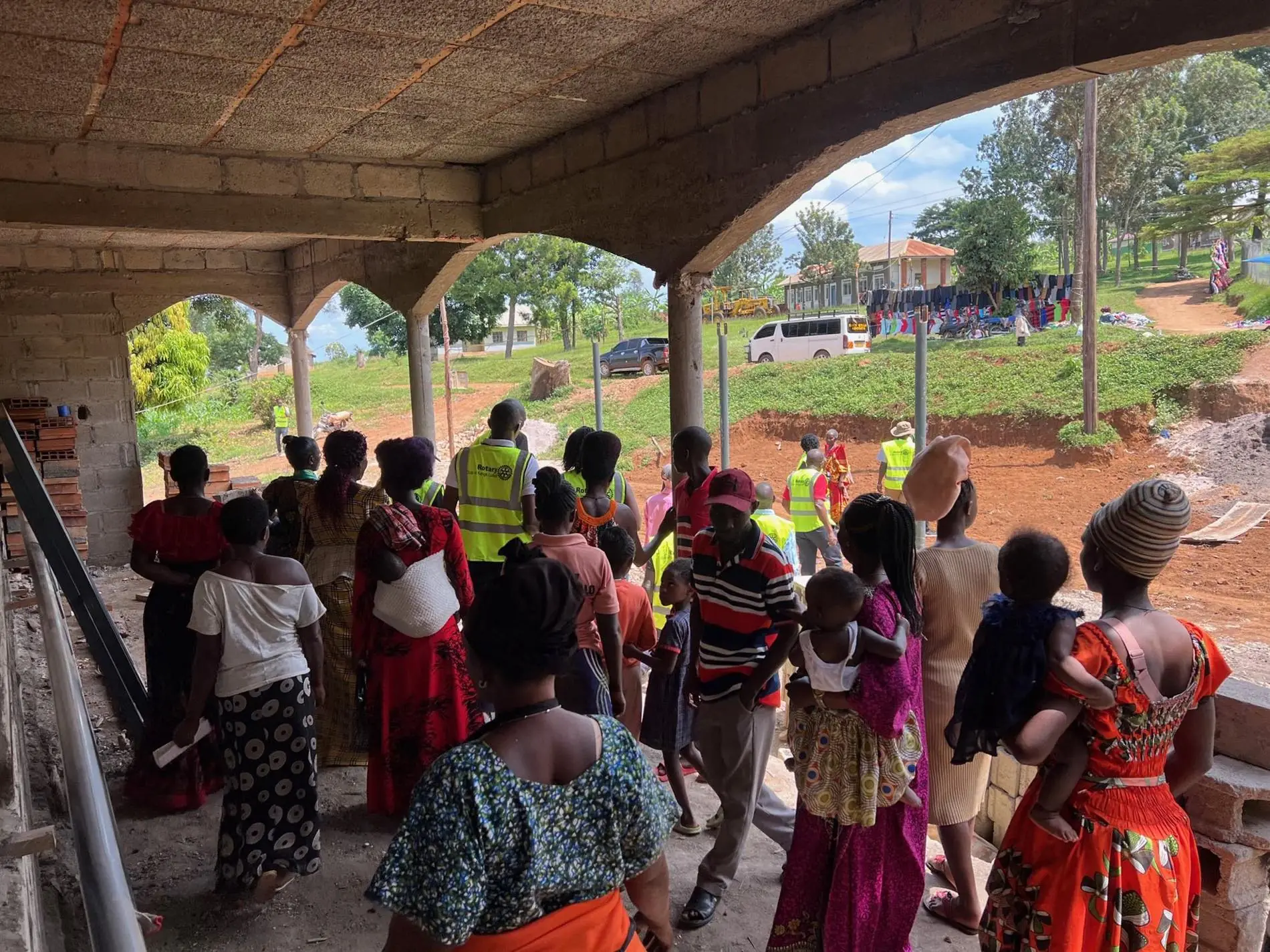 Women and children from the Kyebe community walking through the unfinished maternity clinic during a site visit in October 2024