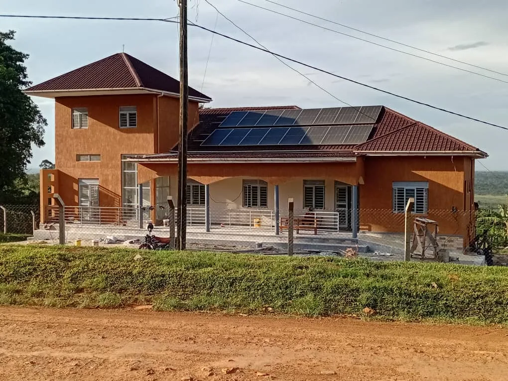 The new clinic today: an orange two-storey building with a tiled roof, solar panels, a covered veranda and a perimeter fence